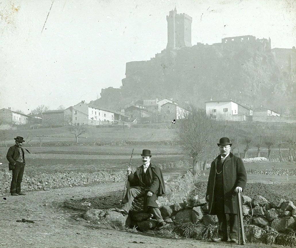 Archives départementales de la Haute-Loire. Collection de plaques photographiques, "Trois hommes en chapeaux devant la forteresse de Polignac" (29 Fi 36).